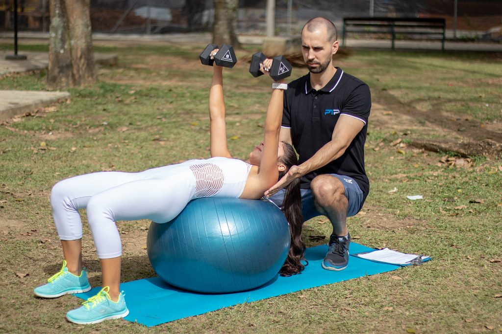 Trainer spotting woman's dumbbell press on ball