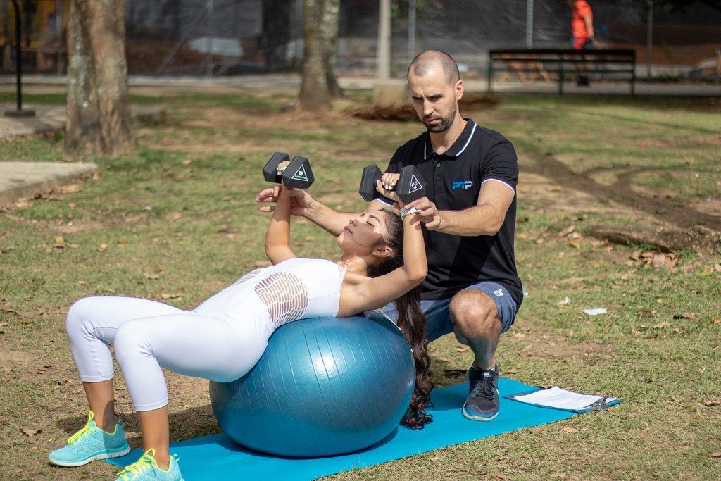Woman doing dumbbell press on ball with trainer