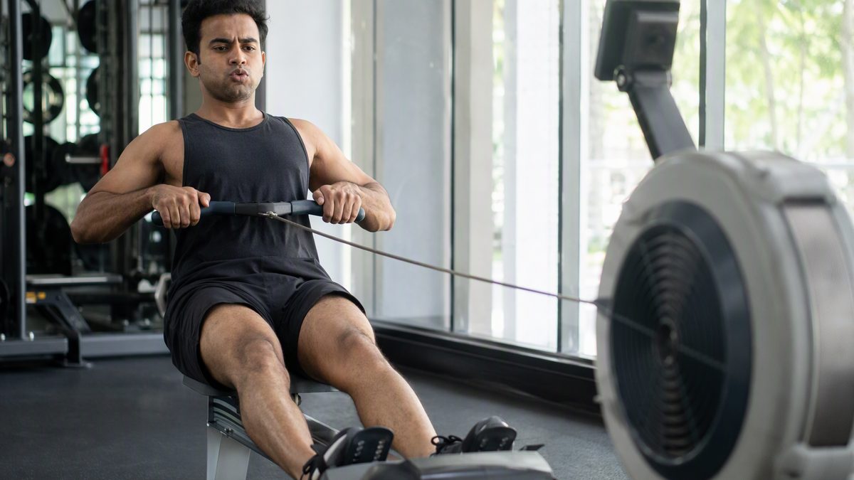 Person rowing hard on an indoor rowing machine in a bright gym